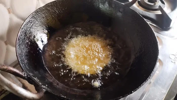 Drop spoonfuls of batter into the hot oil, ensuring not to overcrowd the pan. Do not touch the pitha until it puffs up and floats to the surface.