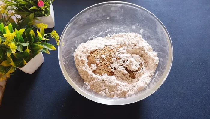 Gradually add the hot melted jaggery to the flour mixture, mixing until a thick batter forms. Add it slowly to prevent lumps. The hotter the jaggery, the softer the gulgule will be.