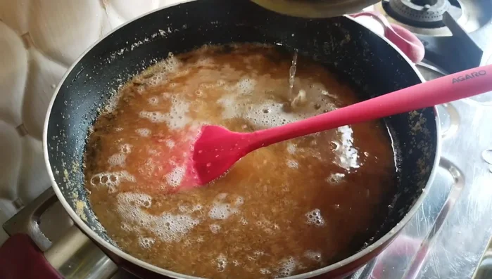 Gradually pour in the prepared syrup, stirring continuously to prevent lumps. Continue stirring until the halwa thickens and leaves the sides of the pan.