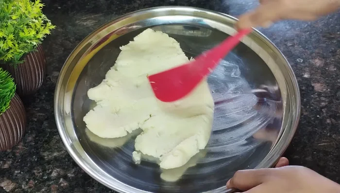 Prepare the dough: Grease a plate with ghee or oil. Spread the semolina dough on the plate while it is still hot. Let it cool for 2-3 minutes. Add 1 tbsp milk powder and mash thoroughly until smooth and not sticky.