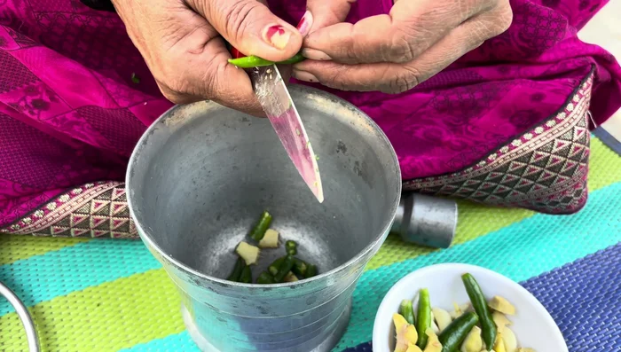 Prepare a paste of ginger, garlic, green chilies, and coriander using a mortar and pestle.