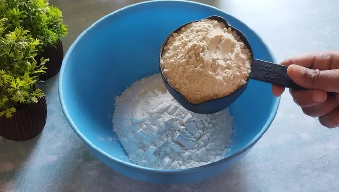 In a bowl, combine refined flour, wheat flour, semolina, grated coconut, sesame seeds, salt, and powdered sugar. Mix well.