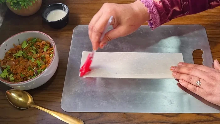 Prepare samosas using readymade samosa sheets. Apply flour paste to one edge, fold into a cone shape, and fill with the cooled onion mixture.