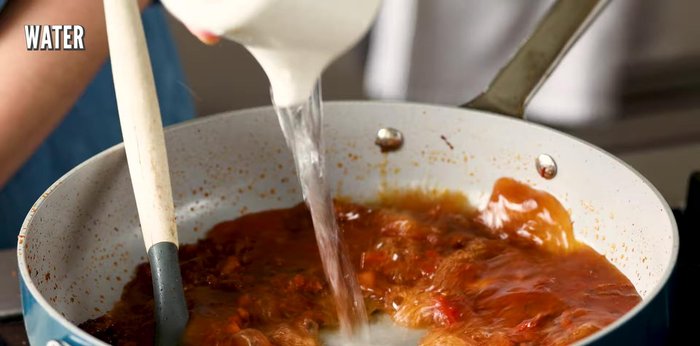 Once the tomato mixture is roasted and shows an oily sheen, add vegetable stock, coconut milk, and salt. Bring to a boil.