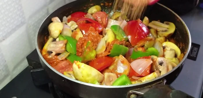 Combine the cooked tomatoes and spices with the fried mushrooms, onion, tomato, and capsicum. Add ground spices, salt, and long-cut green chilies.