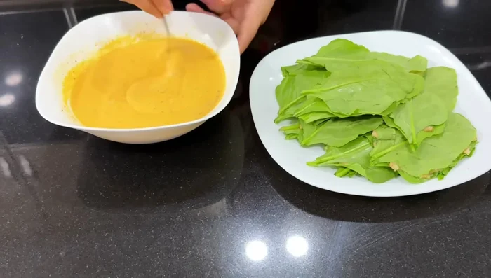Dip the stuffed spinach pakora into the batter, ensuring it's fully coated.