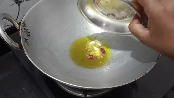 Once the water has dried, add a little more oil, a chopped garlic clove, and half a dried red chili. Fry until fragrant.