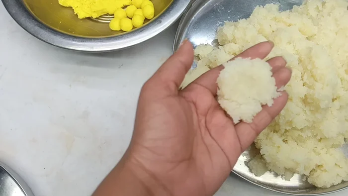 Take some of the cooled coconut mixture, place a mawa ball inside, close it, and shape it into a round ladoo.