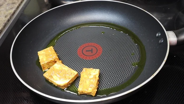 Return the pan to low heat and add the marinated tofu pieces, cooking lightly on one side.