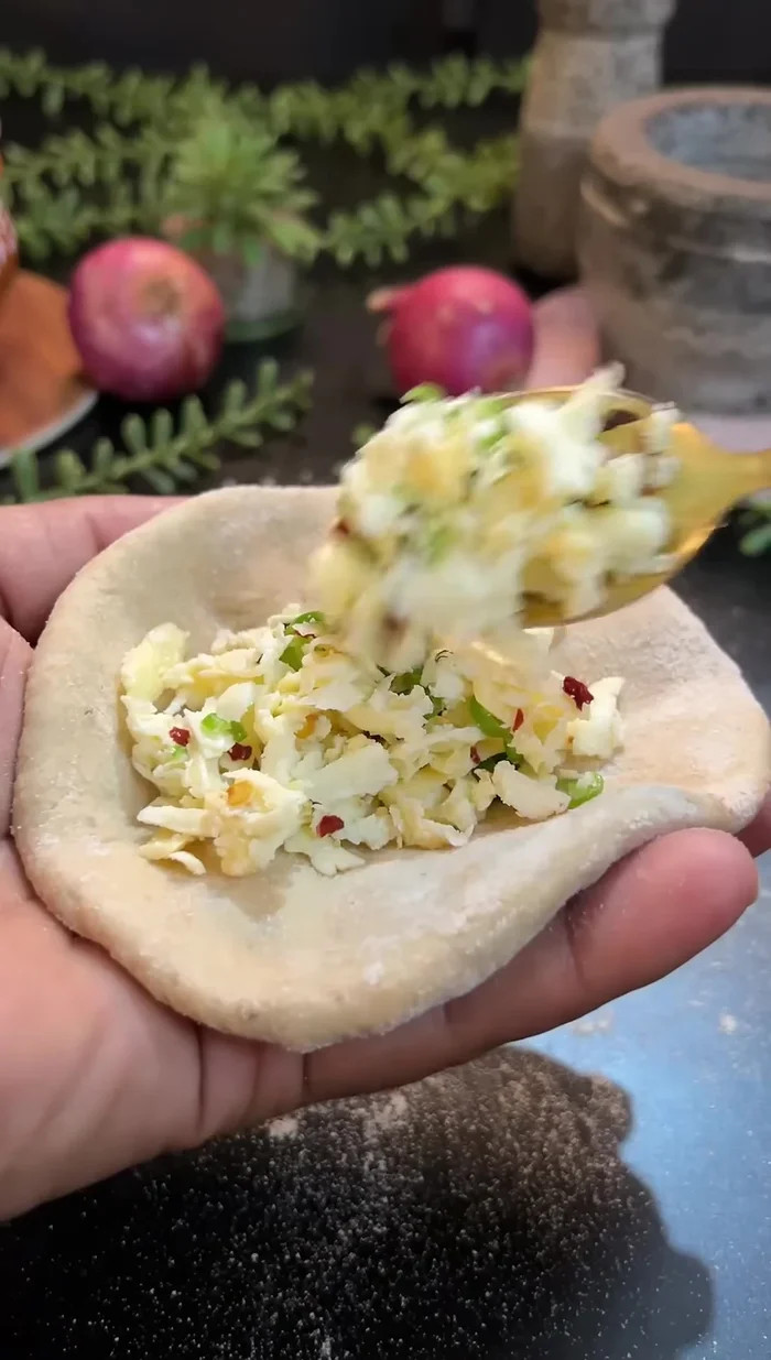Add the paneer stuffing to the center of each flattened dough ball.