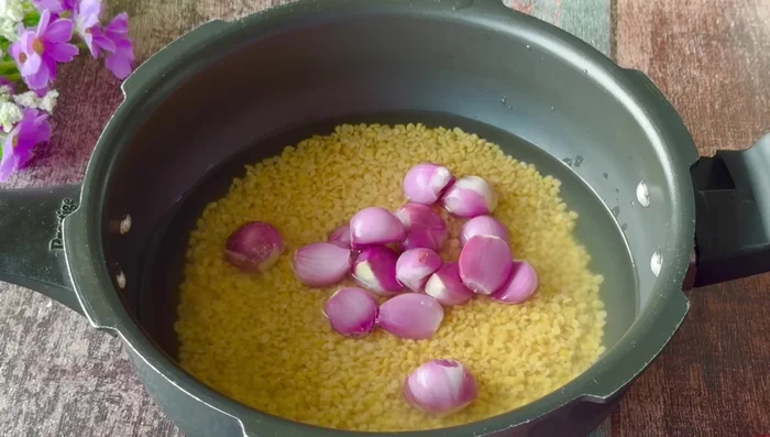 Add small onions (or chopped large onion), chopped tomatoes, garlic, green chilies, turmeric powder, and chopped carrots (if using) to the soaked dal.