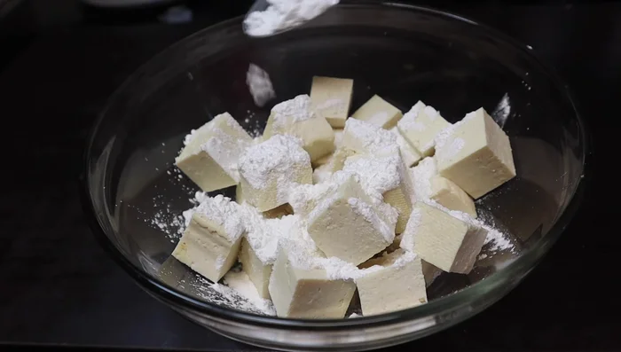 In a bowl, toss the tofu with 2 tablespoons of cornflour, salt, a pinch of black pepper, and optional Kashmiri chili powder. Mix well by shaking the bowl with a plate on top.