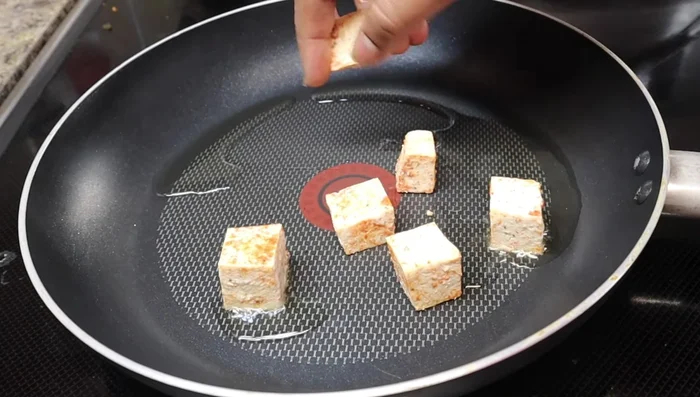Heat 2 tablespoons of oil in a pan over medium heat. Fry the tofu pieces until slightly crispy, stirring occasionally to prevent burning.