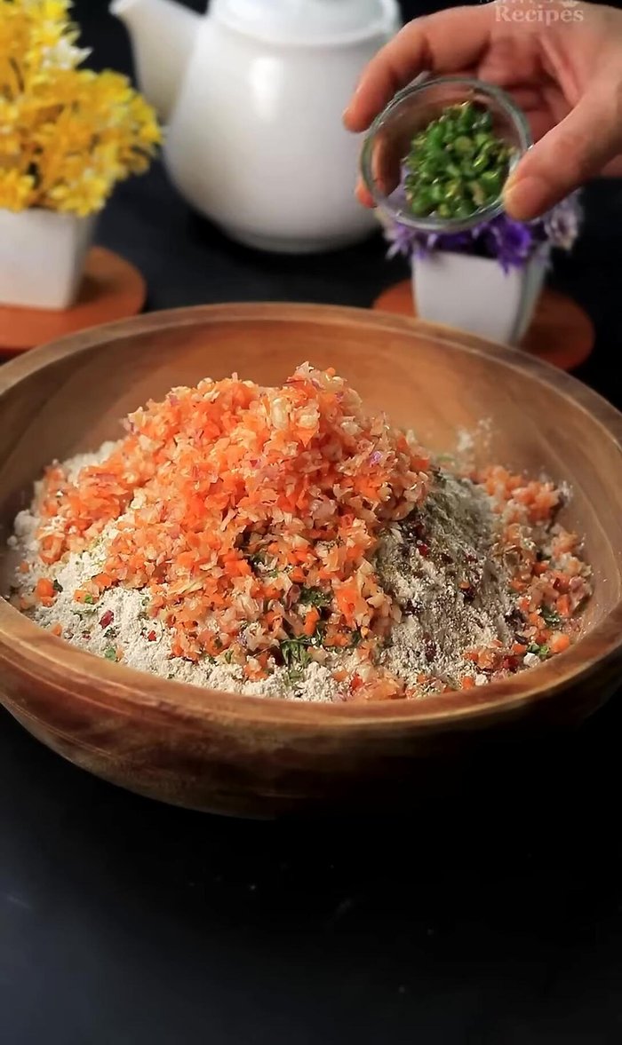 Add the chopped vegetables, green chilies, a pinch of turmeric powder (optional), and chopped coriander leaves to the flour mixture.