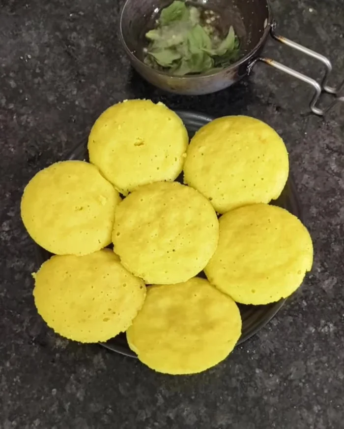 Prepare tadka: Heat oil, add mustard seeds, green chilies, and curry leaves. Once fragrant, pour tadka over the idli dhokla.