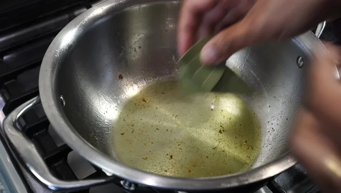 Remove the fried pumpkin and set aside. In the same pot, add a bay leaf, two dry red chilies, and 1 teaspoon of patchon (Bengali five spice). Stir on low heat for a few seconds.