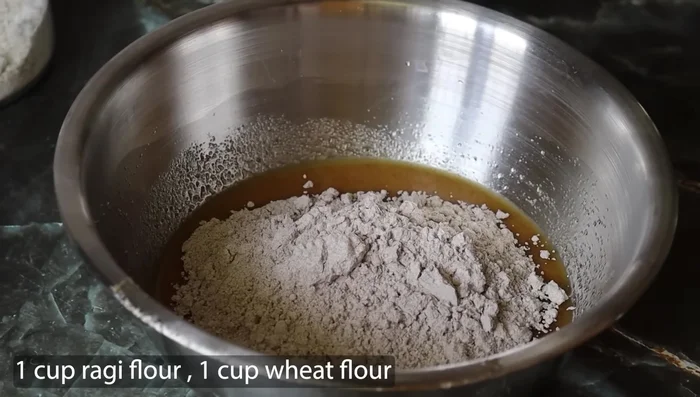 Add 1 cup of ragi flour, 1 cup of wheat flour, 1 teaspoon of cardamom powder, and a pinch of salt. Mix thoroughly.