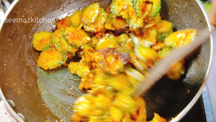 Heat oil in a pan, add mustard seeds and asafoetida. Add bitter gourd and fry, then add onion and the ground spice mixture.