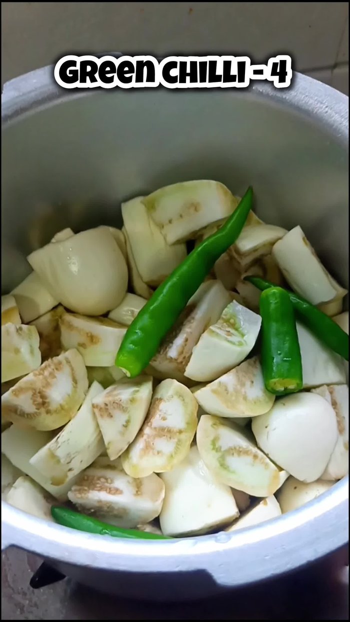 Add green chilies as needed to the brinjal, along with a little water. Cook in a pressure cooker for one whistle.