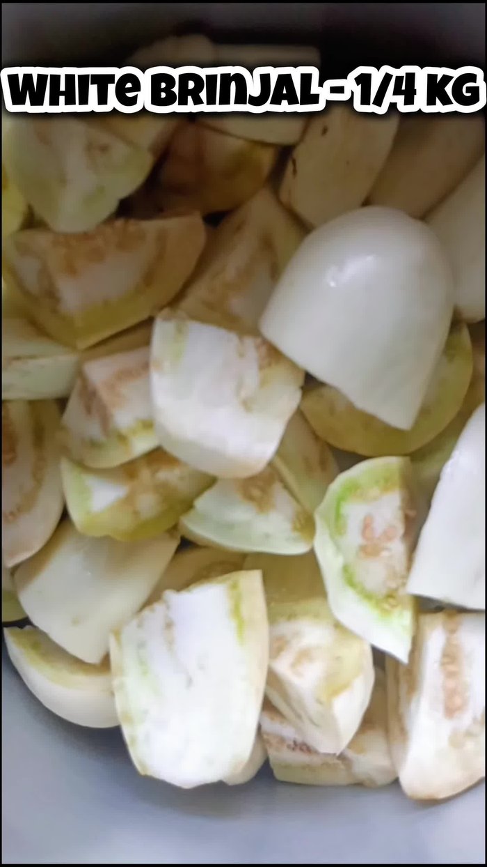 Cut the green portion from the top of the white brinjal and cut it into large pieces, resembling pizza shapes.