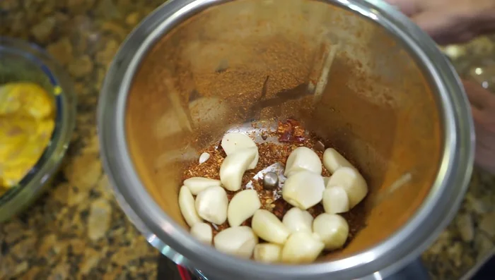 Add garlic to masala: Add the ground garlic to the spice mixture and grind again to a coarse consistency, not a fine paste.