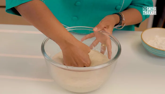 Second proof: Divide the dough into two parts. Shape each into a ball, and place them on a floured tray. Brush with oil and let it rise in a warm place until almost doubled.