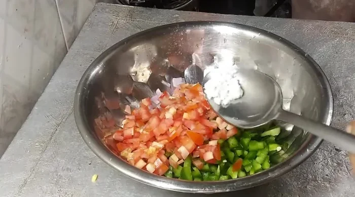 Prepare the vegetable stuffing: finely chop onions, capsicum, and tomatoes. Add salt, chili flakes, black pepper powder, oregano, green coriander, and cheese.