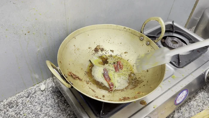 Prepare the gravy in the remaining oil: Add bay leaves, whole red chilies, cumin seeds, and black mustard seeds. Once the mustard crackles, add green chilies and fry until color changes.