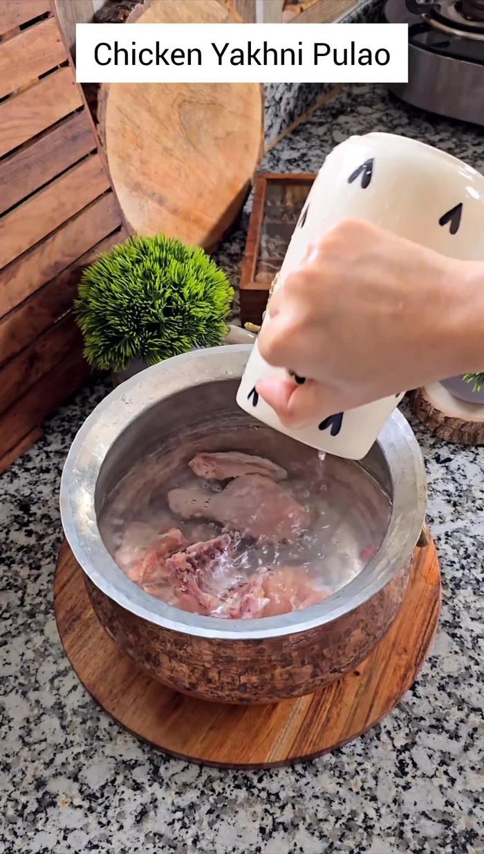 In a heavy-bottomed pan, add chicken, 5 cups of water, bay leaves, cinnamon stick, and the prepared spice mixture. Add ginger, garlic, slit green chilies, and sliced onions. Cook covered over medium heat for 10-15 minutes, until chicken is fully flavored.