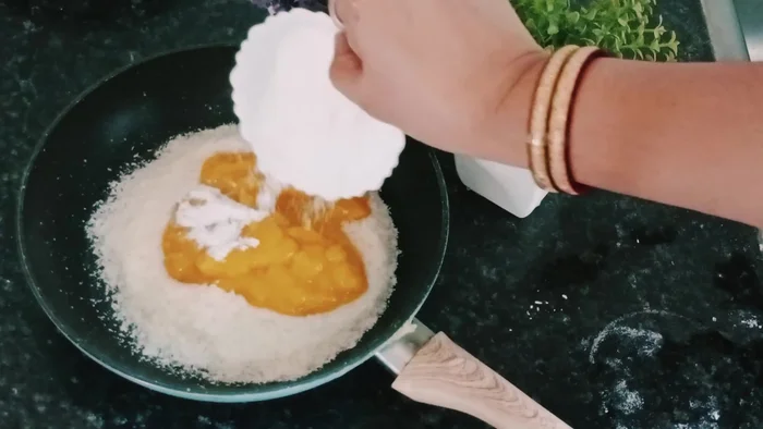Add coconut powder, sugar powder, and mango pulp into a pan.
