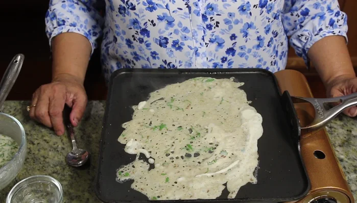 Pour a ladleful of batter onto the hot surface, spreading it thinly to form a dosa.