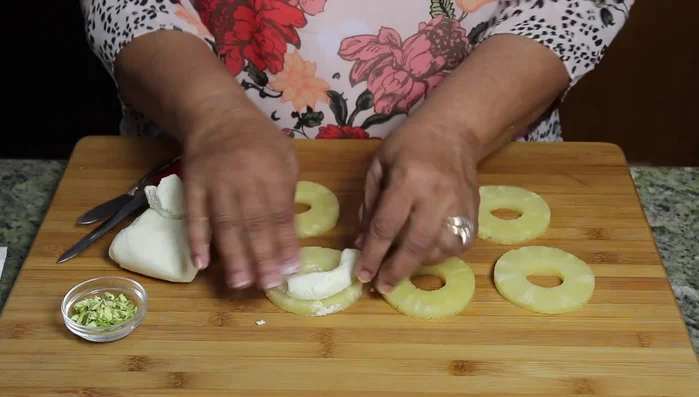 Roll the paneer dough into a log, spread it over the pineapple slices, and cover evenly.