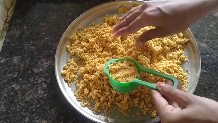 Take a small bowl or cup. Press a portion of the mixture into the bowl, forming a laddu. Gently shape it with your hands.
