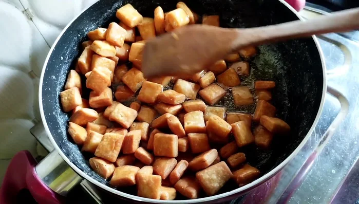 Add the fried shakkarpare to the sugar syrup. Stir gently for 2-3 minutes over low heat, then remove from heat and continue stirring until the sugar candy is coated and separated.