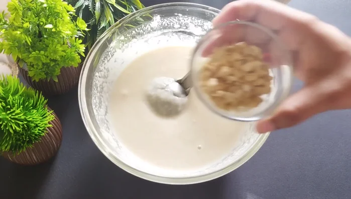 After resting, whisk the batter again to ensure there are no lumps. Add chopped cashews, grated coconut (or desiccated coconut powder), and any other desired dry fruits. Mix well.