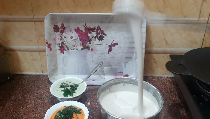 Pour a ladleful of batter onto the hot tawa, spreading it thinly in a circular motion.