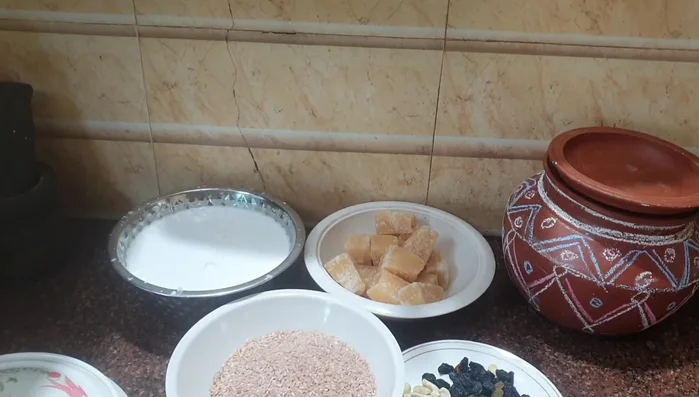 Prepare the ingredients: new rice, jaggery, milk, raisins, cashews, almonds, and ghee.