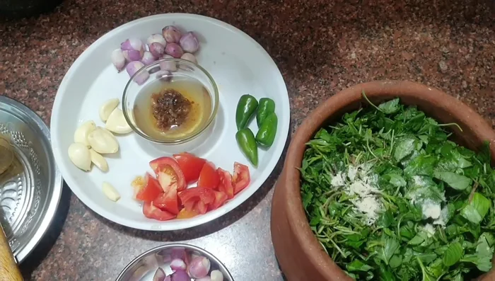 Add turmeric powder, powdered onion, chilies, garlic, and tomato to the greens in the earthen vessel.