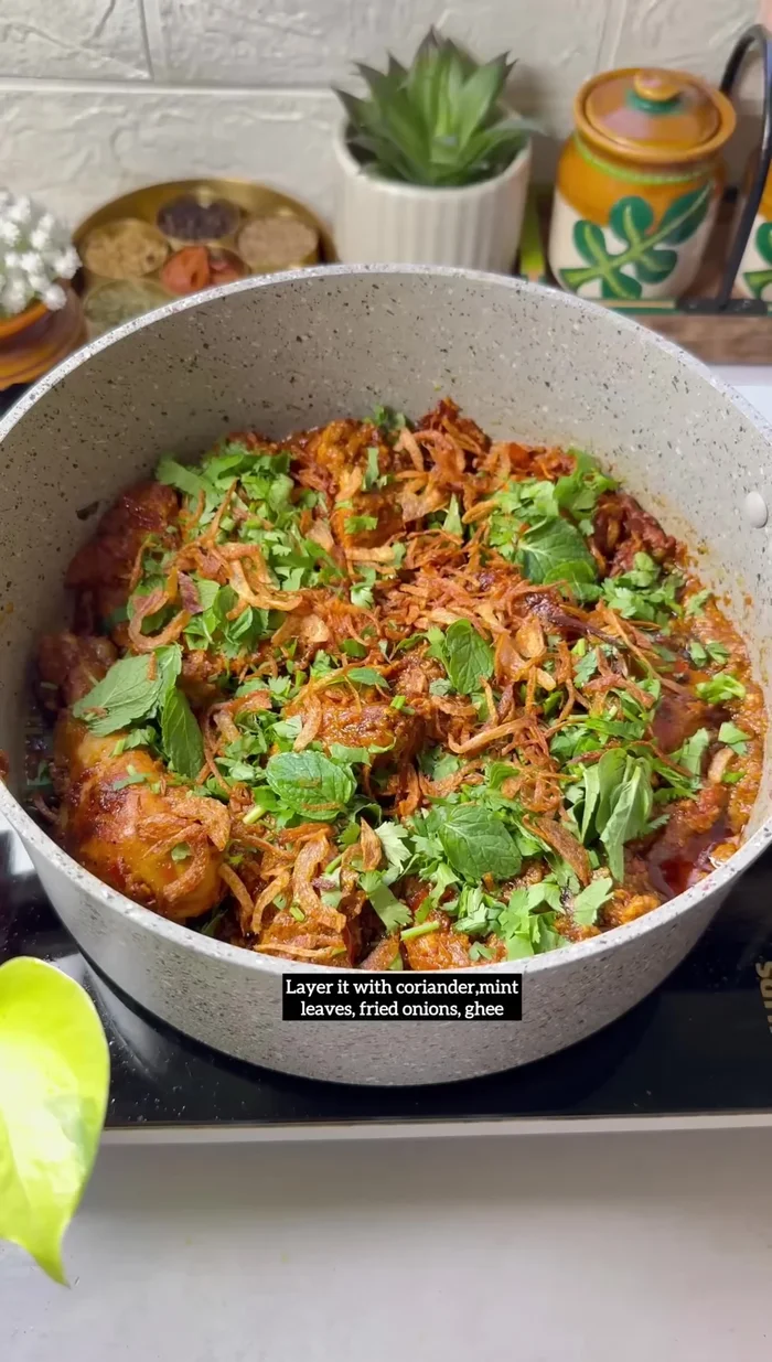 Layer the biryani: Lower the heat and layer the biryani. Start with a layer of the chicken mixture, followed by a layer of rice. Add coriander leaves, mint leaves, fried onions, and ghee. Repeat layers. Top with coriander leaves, mint leaves, ghee, fried onions, and saffron milk.
