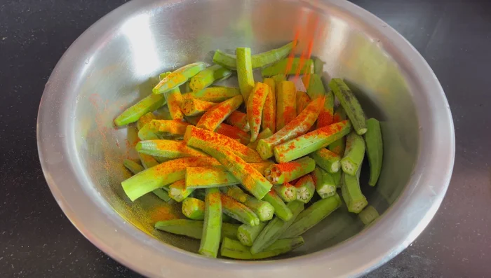 In a mixing bowl, add the chopped ladyfingers, turmeric powder, chili powder, coriander powder, and oil. Mix well and let it rest for 10-15 minutes.