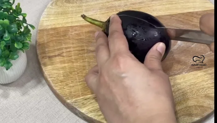 Prepare the brinjal: Wash and cut the brinjal lengthwise, making cuts to create square-shaped boxes. This helps check for worms and ensures even cooking. (100.079)