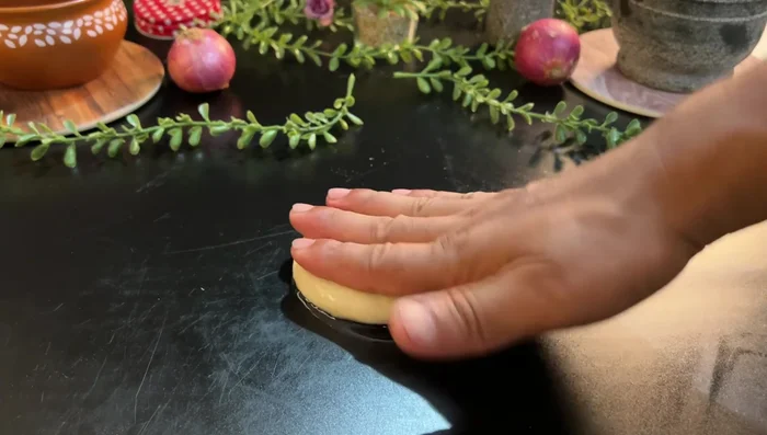 Make peda and pour generous oil on it before rolling. Roll out, add more oil, fold it in layers, and then into a roll. Press gently, and roll again lightly.