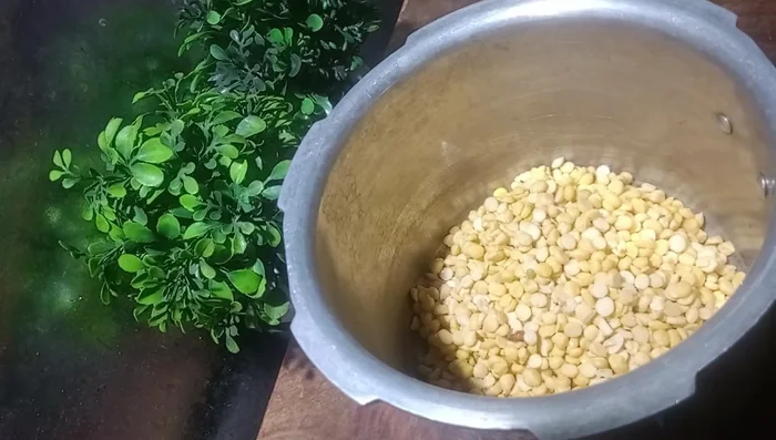 Transfer the soaked dal to a cooker. Add water, chopped onions, turmeric powder, red chili powder, garlic, and chopped tomatoes.