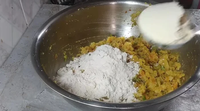 Combine poha mixture with some of the cooked vegetables, wheat flour, gram flour, and water to form a thick batter.