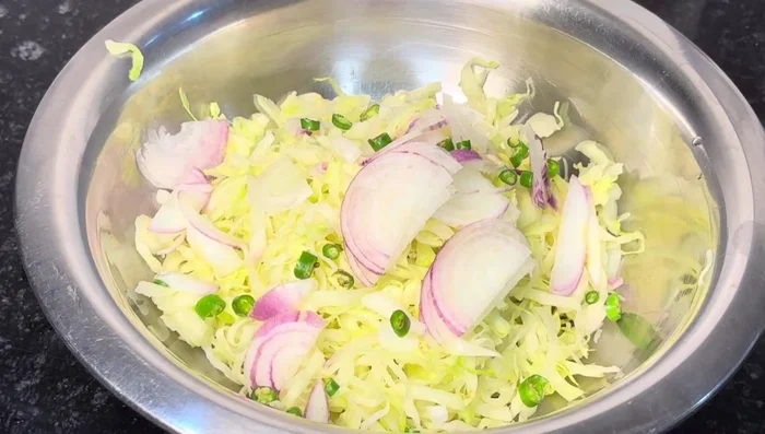 In a bowl, combine the squeezed cabbage, chopped onion, green chilies, and coriander leaves (235.68).