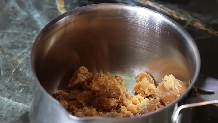 In a saucepan, add 1 cup of powdered jaggery and 2 cups of water. Heat on high flame until the jaggery dissolves and boils, mixing constantly.
