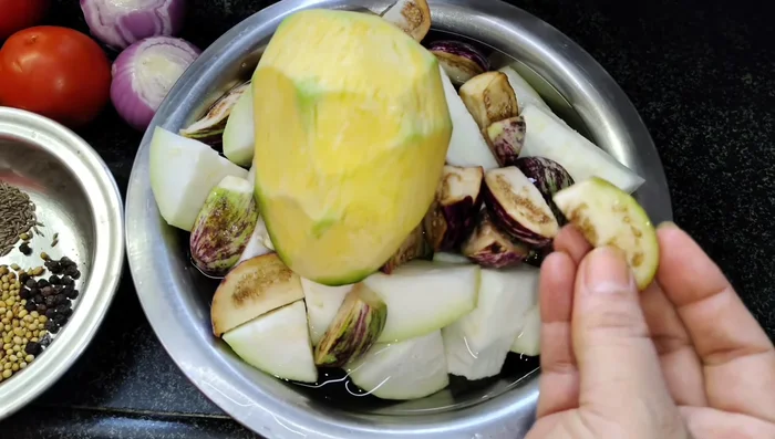 Prepare vegetables (brinjal, doodi, optional cauliflower, pumpkin, raw mangoes). Wash and immediately submerge in water to prevent darkening. (131.76)