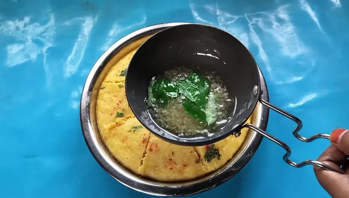 Prepare tempering: Heat oil, add sugar, curry leaves, and a little salt and water. Pour this tempering over the dhokla.