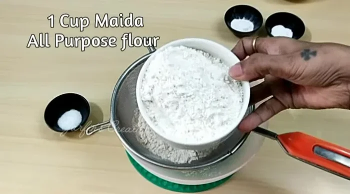 Sift 1 cup of wheat flour (atta) and 1 cup of all-purpose flour (maida). Add salt, baking soda, and baking powder. Mix well.