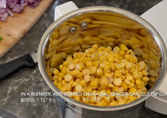 In a blender, add soaked chana dal, chopped ginger and garlic, cumin seeds, fennel seeds, dry red chilies, salt, and turmeric powder. Blend into a thick, coarse paste, adding a little water.